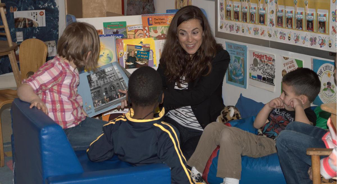 Samantha Richardson reads a book to a group of three children who are seated on the floor in a circle around her.
                  
