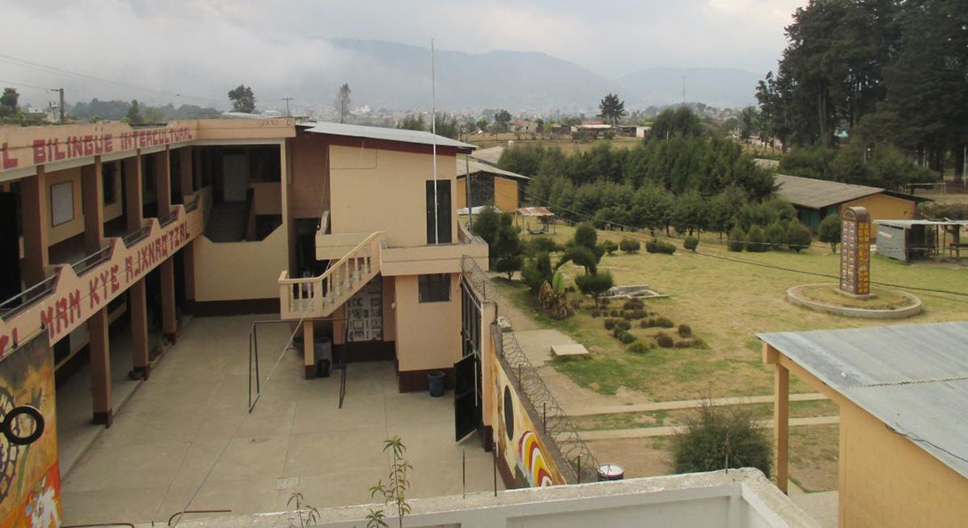 A school building and its courtyard in Guatemala, with mountains in the background and low clouds and fog shrouding the view of the mountains.