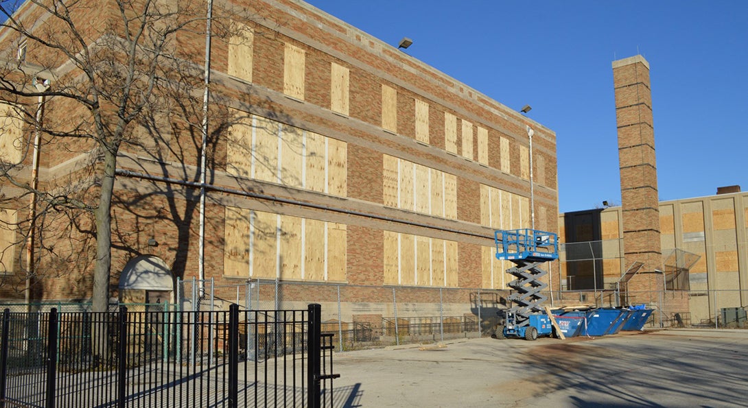 A closed CPS school has its windows and doors boarded with plywood, and a retractable crane platform sits outside the building.
                  