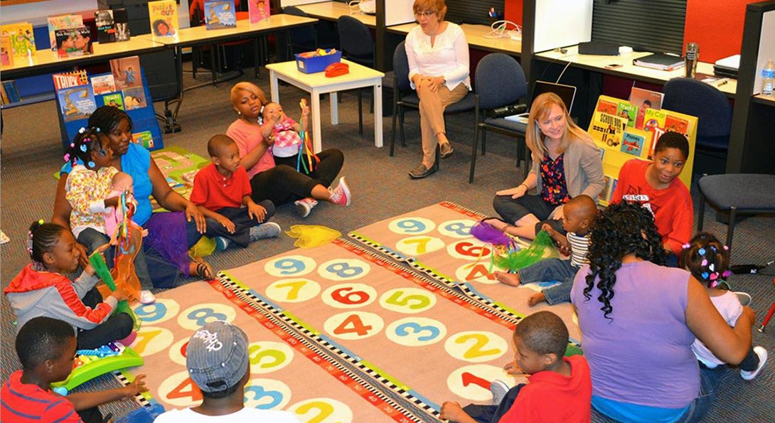 Doctoral student leads a literacy workshop with young mothers, who are seated in a circle with Colleen and singing a rhythmic song to their children.