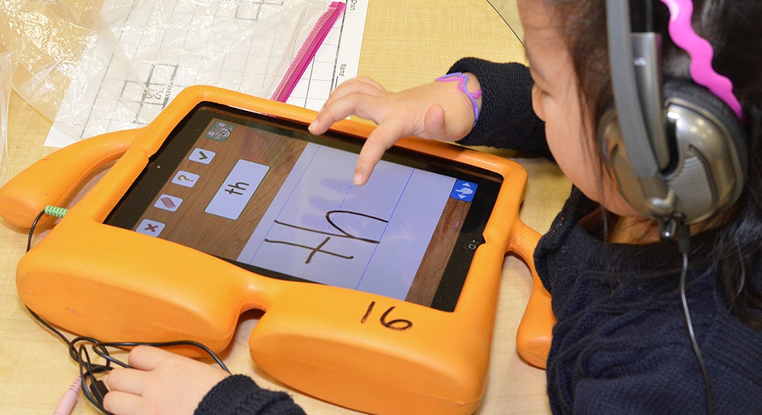 A kindergartner uses her finger to spell out the word 