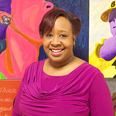 Carlitta Tucker-Powell poses for a photo standing against a colorful mural at Gwendolyn Brooks College Prep.