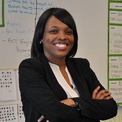 Janice Jackson stands with her arms folded, posing for a photo in a Chicago Public Schools classroom.  Behind her is a whiteboard with instructions for students written in marker.