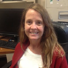 Jennifer Asimow poses for a photo, sitting at a desk with a computer behind her.