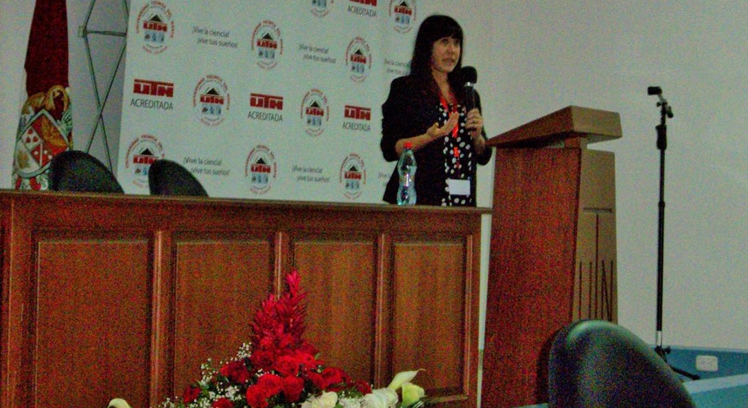 Alumna Alexis Cullerton stands behind a podium holding a microphone delivering a speech to educators in Educador on English education for teachers.
                  