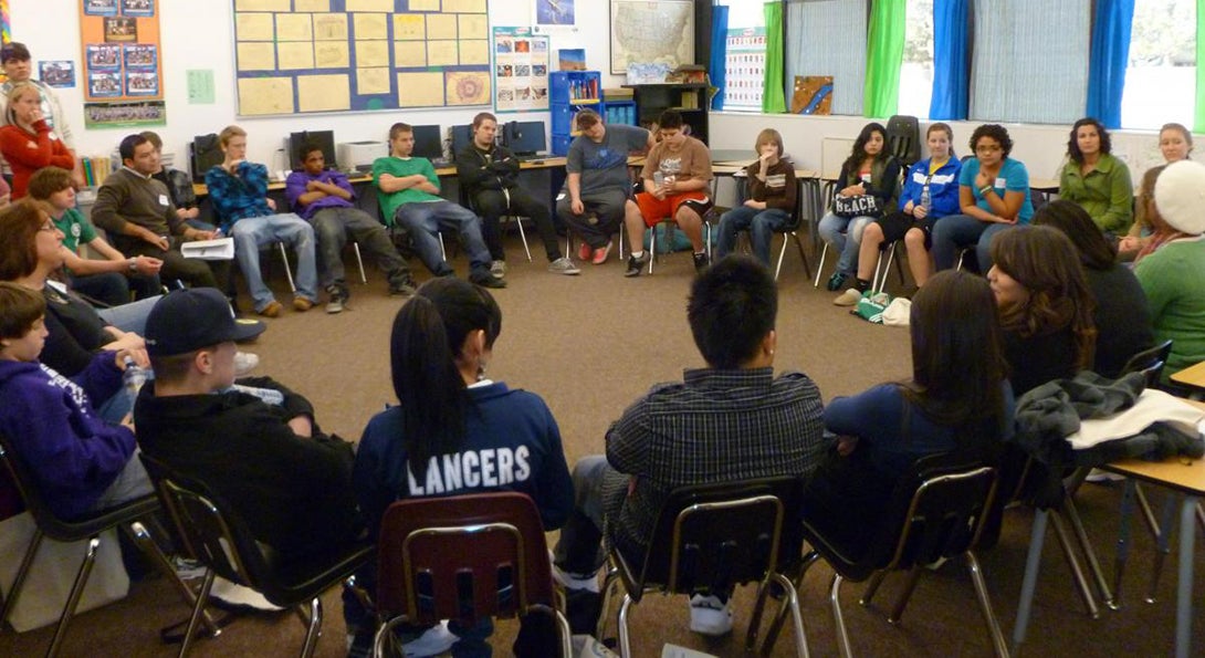 In a classroom, about 30 students sit in a peace circle, seeking to resolve inter-personal conflicts through peaceful means.
                  