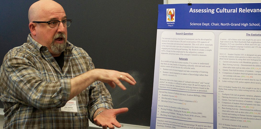 Master Teaching Fellow Phil Cantor gestures with both hands while standing in front of her poster, explaining his research.