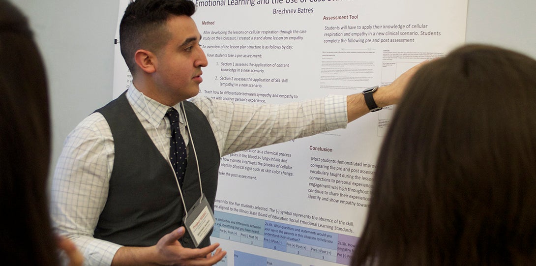 Master Teaching Fellow Brehznev Batres points to a poster detailing his research as SEEEC teaching fellows listen to his presentation.