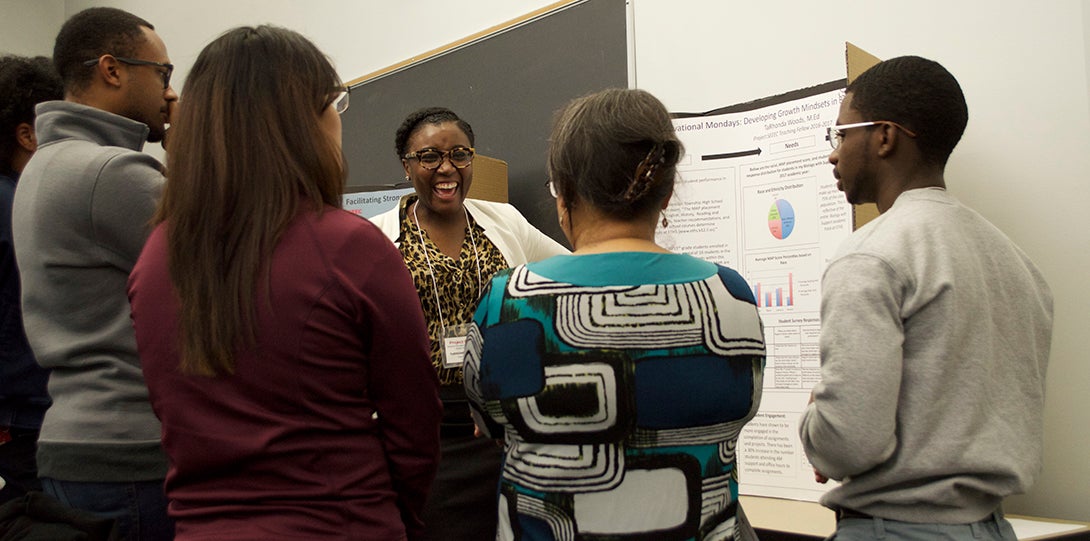 A group of SEEEC teaching fellows stand in front of a poster, having a conversation about the research presented.