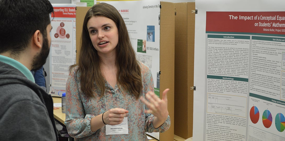 SEEEC Teaching Fellow Melanie Butler gestures with her hands while explaining her poster presentation to another fellow.
