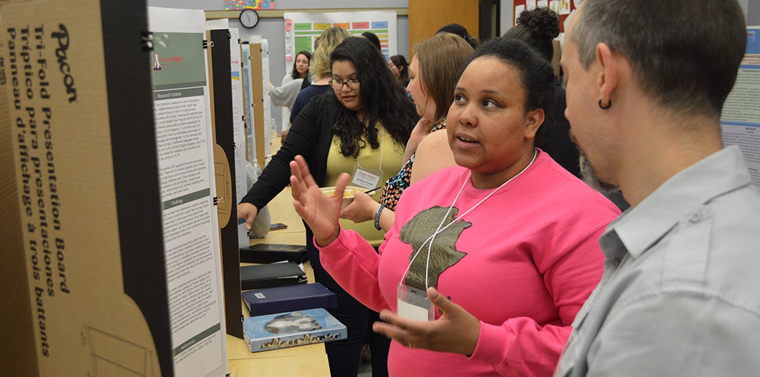 SEEEC Teaching Fellow Michele Drayton gestures with her hands while explaining her poster presentation to professor Danny Morales-Doyle.