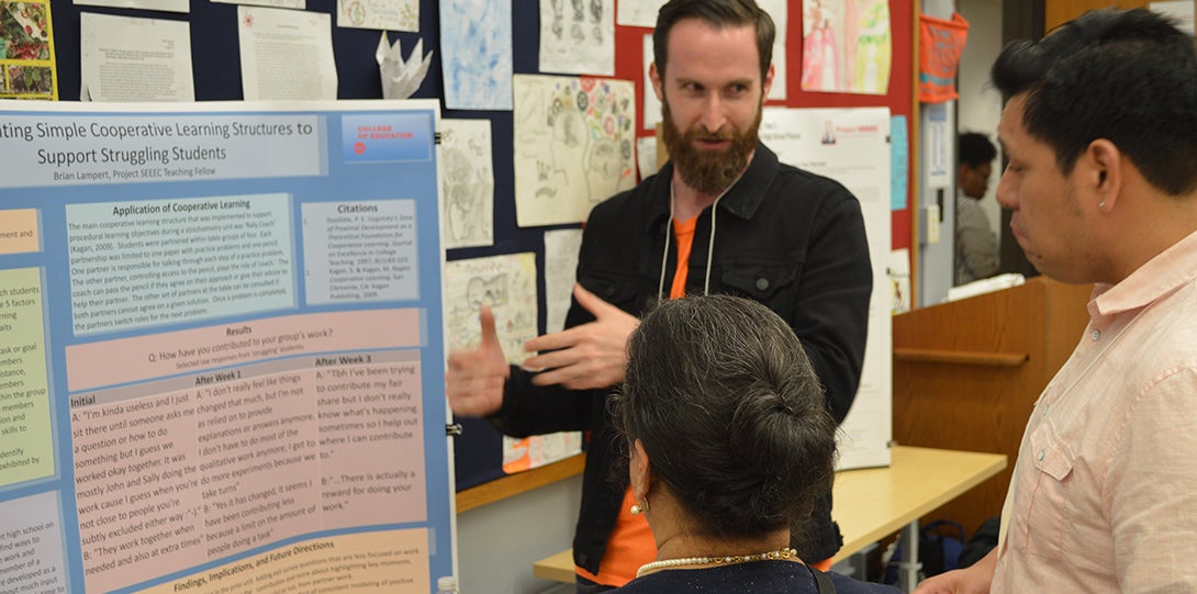 SEEEC Teaching Fellow Brian Lampert gestures with her hands while explaining her poster presentation to other fellows.
