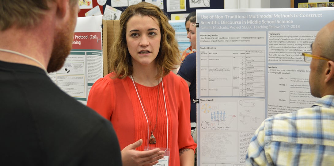 SEEEC Teaching Fellow Natalie Machado gestures with her hands while explaining her poster presentation to another fellow.