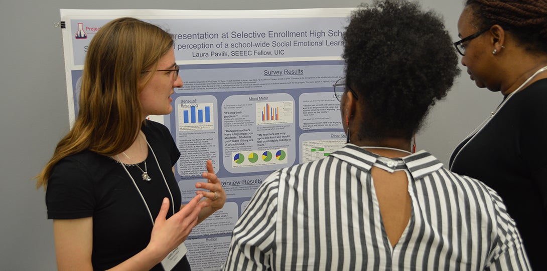 SEEEC Teaching Fellow Laura Pavlik gestures with her hands while explaining her poster presentation to other fellows.