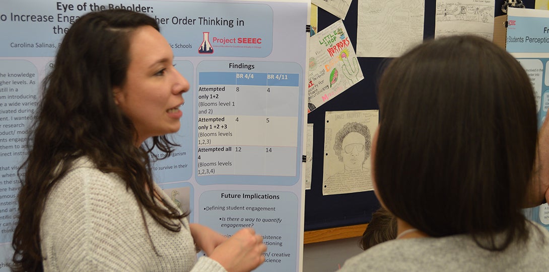 SEEEC Teaching Fellow Carolina Salinas converses with other fellows while standing in front of her poster presentation.