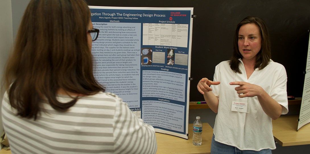 SEEEC Teaching Fellow Mary Segreti gestures with her hands while explaining her poster presentation to another fellow.
