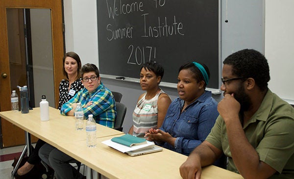 Doctoral alumni and college faculty sit at a table at the front of a classroom, leading a discussion during a PhD Special Education summer institute.